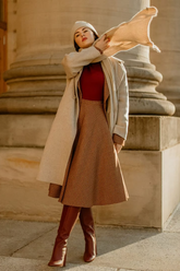 a lady in a red knit top, a brown plaid skirt and a beige long wool coat